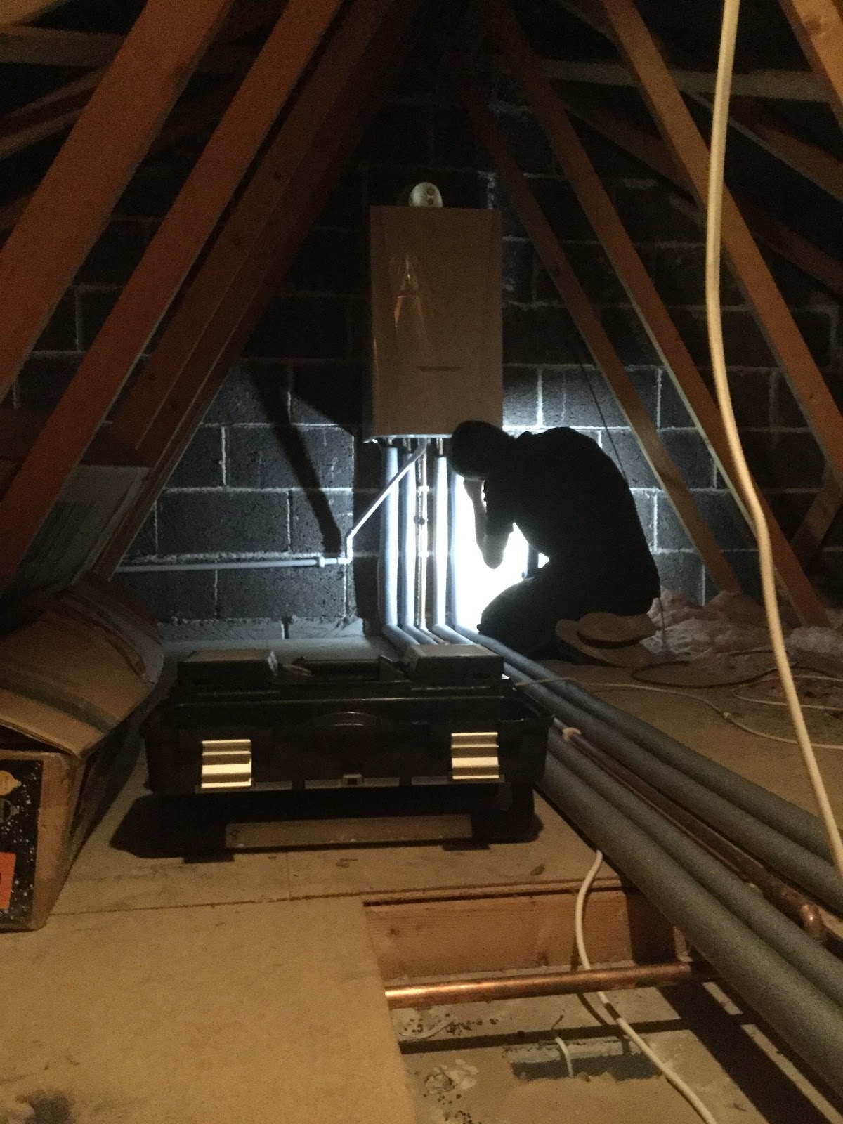 An engineer working on pipework beneath a boiler in a loft